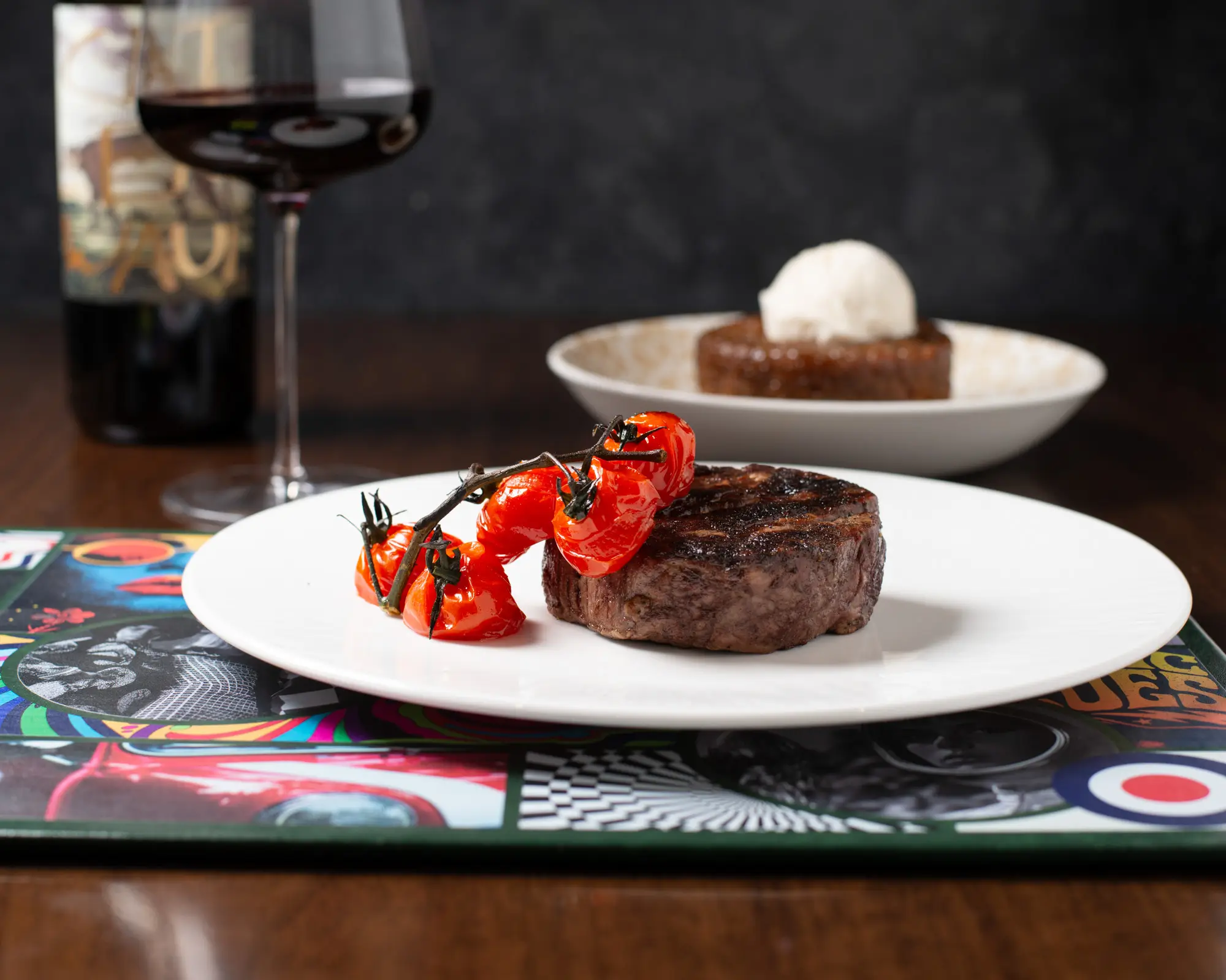 A large filet garnished with roasted tomatoes with a glass of wine