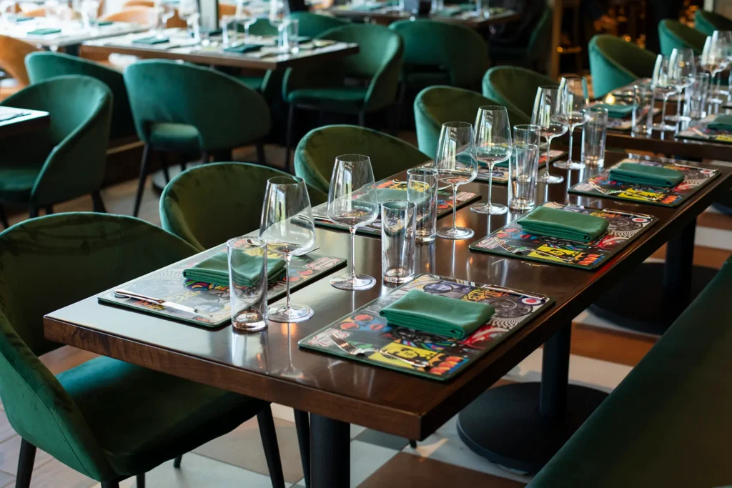 Set dining table at Gordon Ramsay at The Carnaby with green upholstered chairs, colorful placemats, glassware, and folded napkins.
