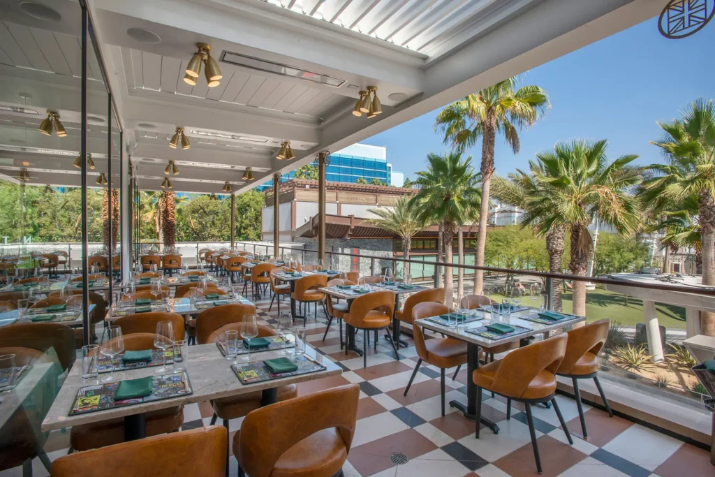 Outdoor terrace at Gordon Ramsay at The Carnaby with tan seating, set dining tables, and views of palm trees at Downtown Disney.