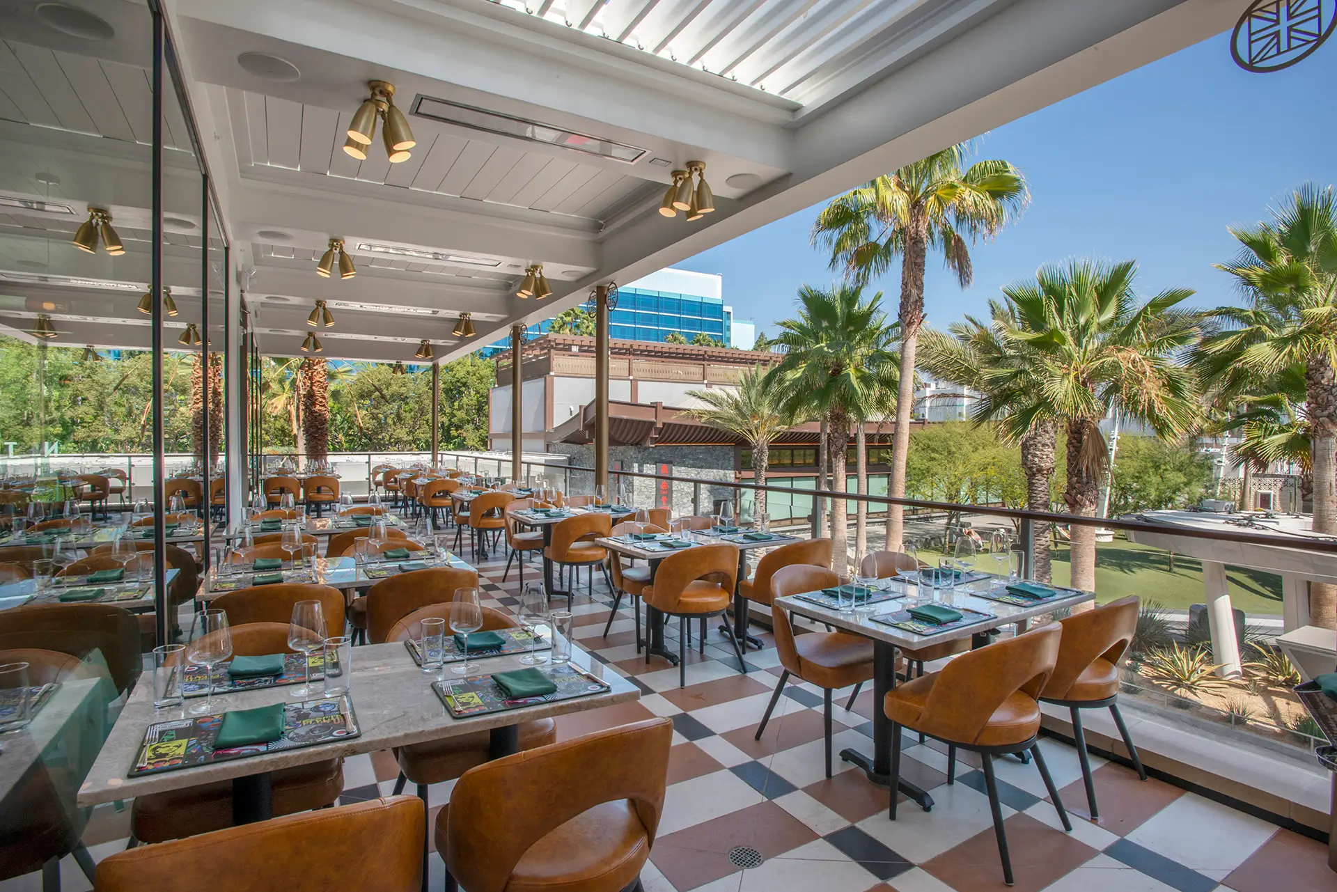 Outdoor dining terrace at Gordon Ramsay At The Carnaby with set tables, leather chairs and views of palm trees at Downtown Disney.