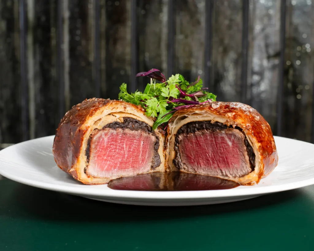 Beef Wellington at Gordon Ramsay at The Carnaby, sliced to reveal medium-rare beef wrapped in mushroom duxelles and golden puff pastry.