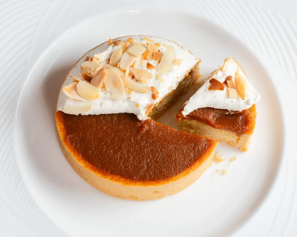 Pumpkin Bakewell Tart with pumpkin filling, whipped cream and toasted almonds, served on a white plate.